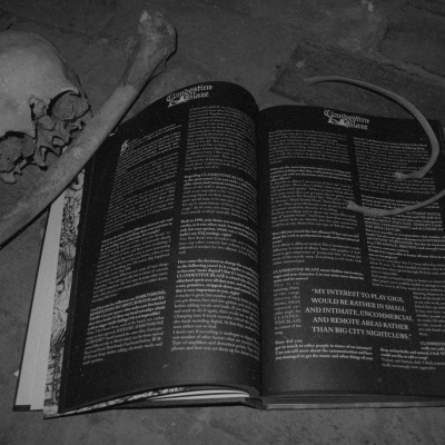 Livro aberto com texto em fundo preto, crânio humano e osso ao lado numa superfície de pedra