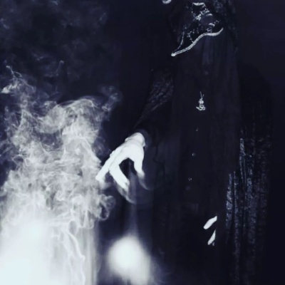 Figura fantasmagórica com capa preta longa e mão branca estendida em ambiente com névoa