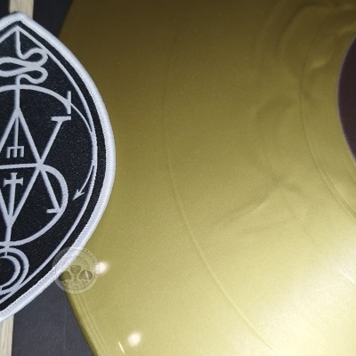 Disco de vinil dourado com etiqueta preta e distintivo bordado preto e branco