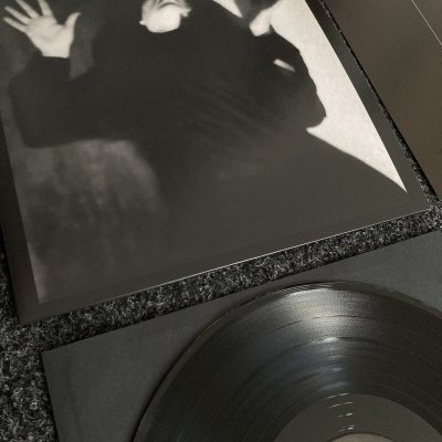Disco de vinil preto com capa com imagem em preto e branco de pessoa numa pose dramática