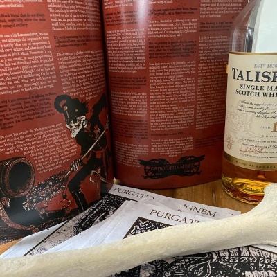 Garrafa de whisky Talisker com revista aberta e charuto branco sobre madeira