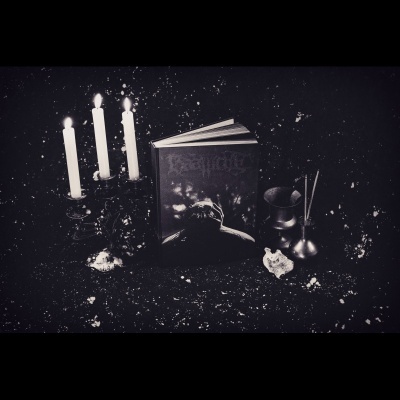 Livro 'Ravnør' aberto com velas acesas e objetos metálicos numa superfície preta manchada