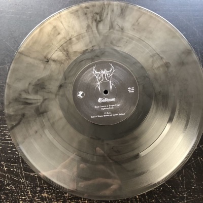 Disco de vinil translúcido marmoreado cinza e preto com etiqueta central preta e texto branco.