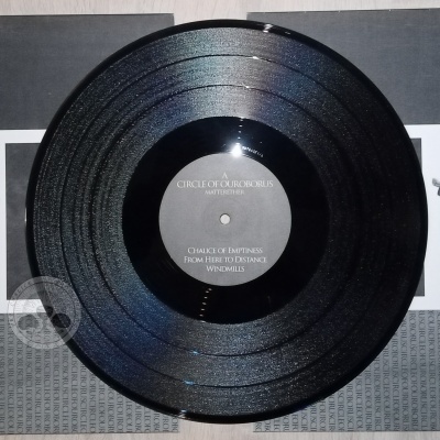 Disco de vinil preto sobre capa tripla com imagens monocromáticas e texto central no vinil