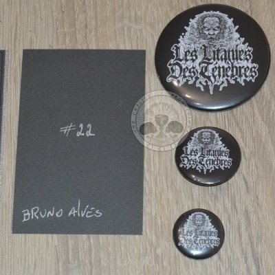 Cartões cinza escuro com texto e vários bottons pretos e brancos com ilustrações e texto Les Litanies Des Tenebres sobre superfície de madeira clara.