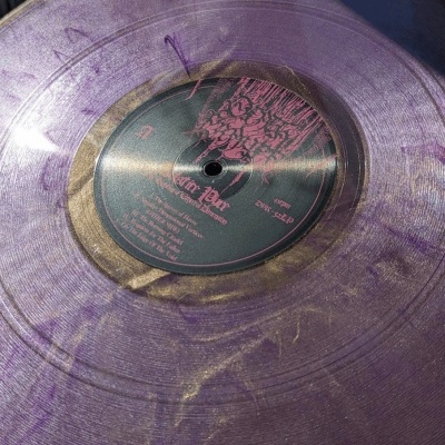 Disco de vinil translúcido roxo e dourado com etiqueta preta e rosa
