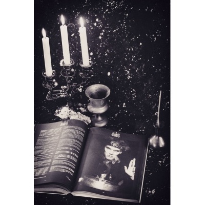 Castiçal de três velas, cálice metálico e livro aberto com fotografia em fundo escuro