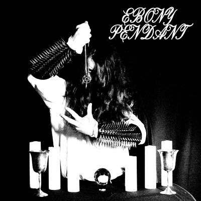 Pessoa com pendente de pentagrama e braçadeiras com spikes em ambiente com velas e cálices