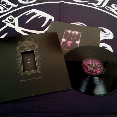 Vinil preto com capa preta e detalhes roxos, texto The Three Tremendous Lies, sobre superfície preta e branca