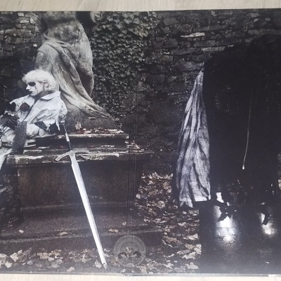 Capa de álbum com foto de figuras encapuzadas em ambiente externo rústico.