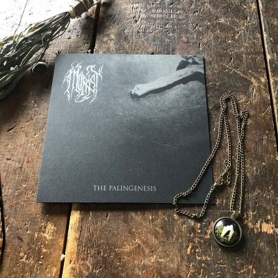 Capa de CD preta com texto THE PALINGENESIS e colar com pendente redondo sobre madeira