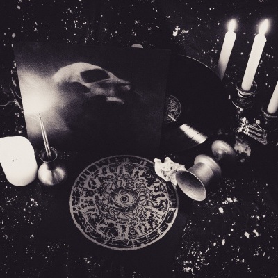 Vinil com capa escura, vela branca, candelabro com três velas e placa decorativa redonda