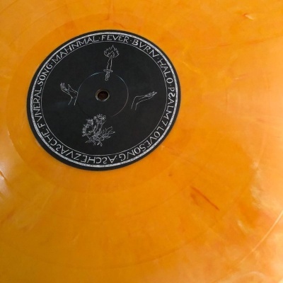 Disco de vinil laranja translúcido com etiqueta preta e texto branco circular.