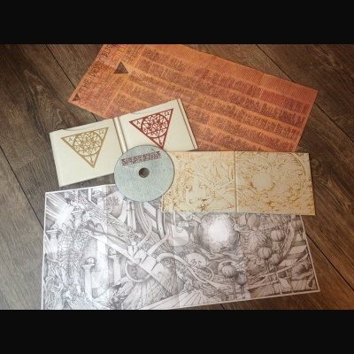 Conjunto de CD com estojo, disco, folhas ilustradas e mapas, sobre chão de madeira.