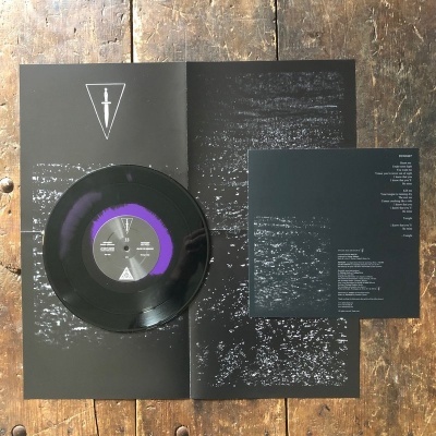 Vinil preto com etiquetas roxa e preta, poster e folha preta com texto branco sobre mesa de madeira