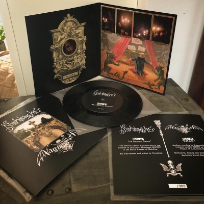 Disco de vinil preto com capa ilustrada e folhas de texto em preto e branco sobre mesa cinza