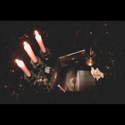 Velas acesas, livro aberto, CD e objeto branco sobre mesa escura