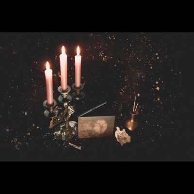 Candelabro com velas cor de rosa acesas, cartão postal, caixa preta, vaso dourado com incenso e coral sobre fundo preto