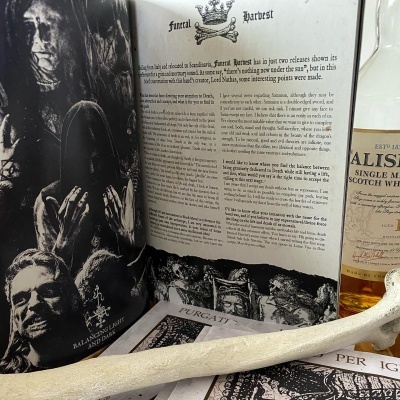 Página de revista aberta com texto e imagens em preto e branco, garrafa de whisky e osso branco sobre folhas de papel.