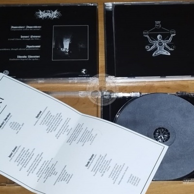 CDs com capas negras, CD cinza e folha branca com letras de músicas sobre mesa de madeira