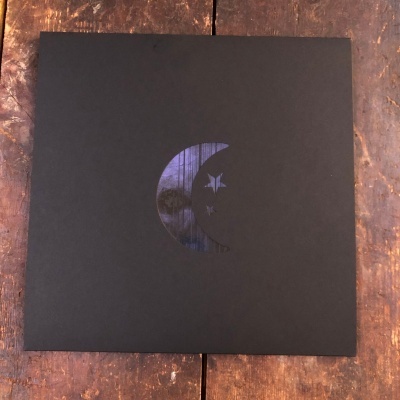 Capa preta quadrada com recorte de lua e estrela azul escura sobre madeira