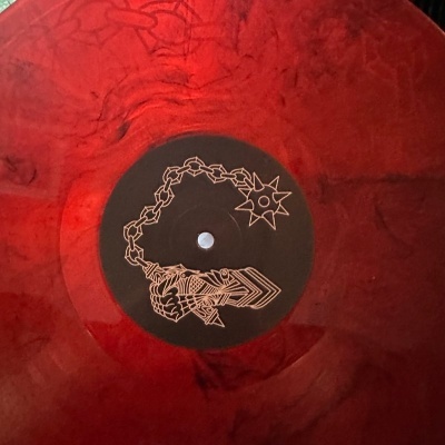 Disco de vinil vermelho translúcido com rótulo preto e arte branca no centro.