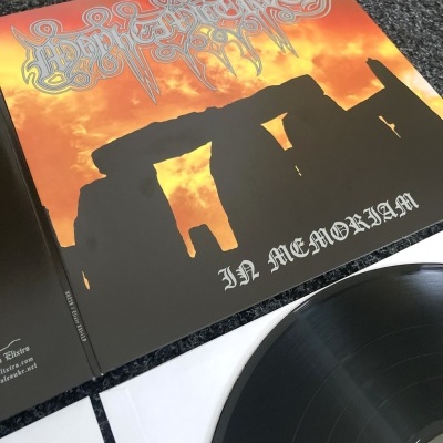 Disco de vinil preto com capa com imagem de Stonehenge e texto IN MEMORIAM