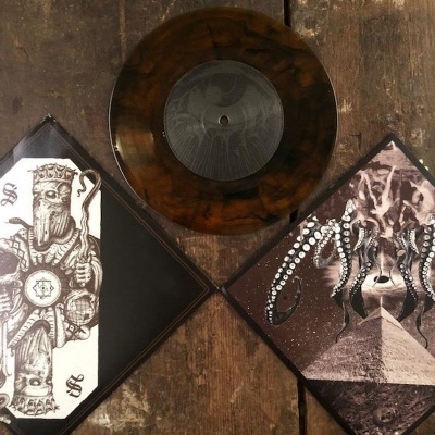 Disco vinil castanho e duas capas de discos lado a lado sobre madeira