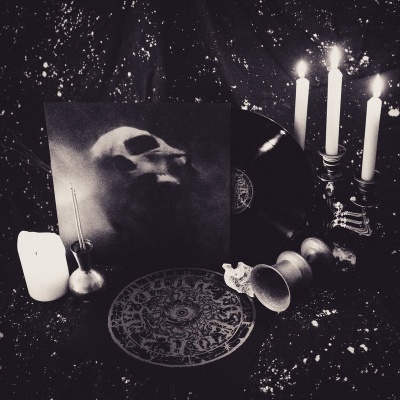 Disco de vinil com capa de caveira, castiçal com velas, e objetos em forma de caveira sobre superfície escura