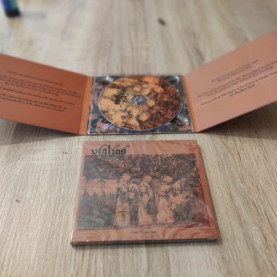 CD de capa dupla aberta e uma capa fechada com arte em tons terrosos em cima de mesa de madeira.