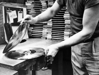 Pessoa a manusear discos vinil num ambiente de trabalho com caixas empilhadas ao fundo