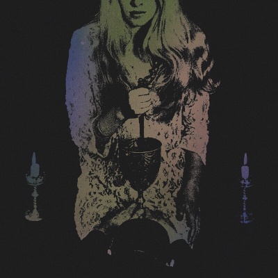 Mulher loira segurando taça escura entre duas velas acesas