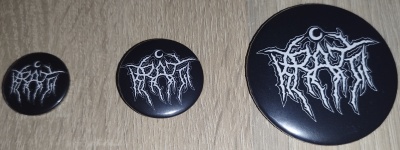 Três bottons pretos com logotipos brancos em superfície de madeira clara