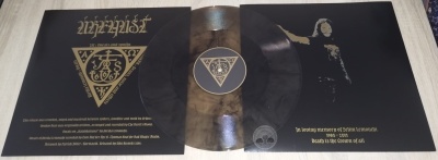 Vinil preto com desgaste dourado, capa preta e dourada com símbolos e texto em espanhol.