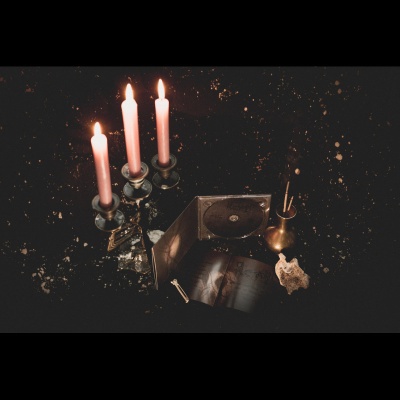 Castical com três velas cor-de-rosa acesas, objeto redondo em suporte aberto e decoração sobre superfície preta manchada de dourado.