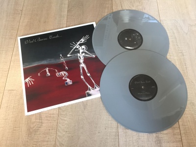 Álbum vinil 'Del Barrio Suelo' com capa artística e dois discos vinis cinzentos sobre mesa de madeira.