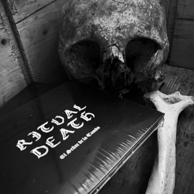 Caveira e osso com livro embrulhado preto com texto RITUAL DEATH em superfície de madeira