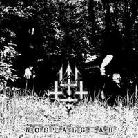 Imagem a preto e branco de duas figuras em negro junto a símbolos em madeira sobre relvado e arbustos ao fundo