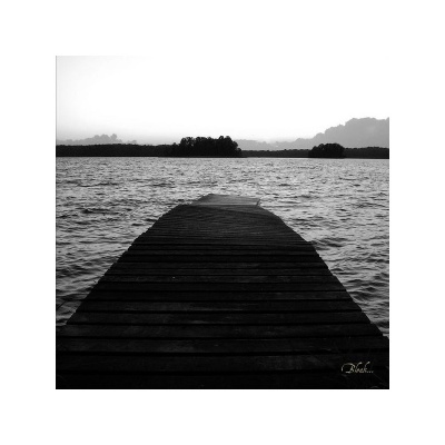 Imagem preto e branco de um cais de madeira sobre a água com ilhas ao fundo.
