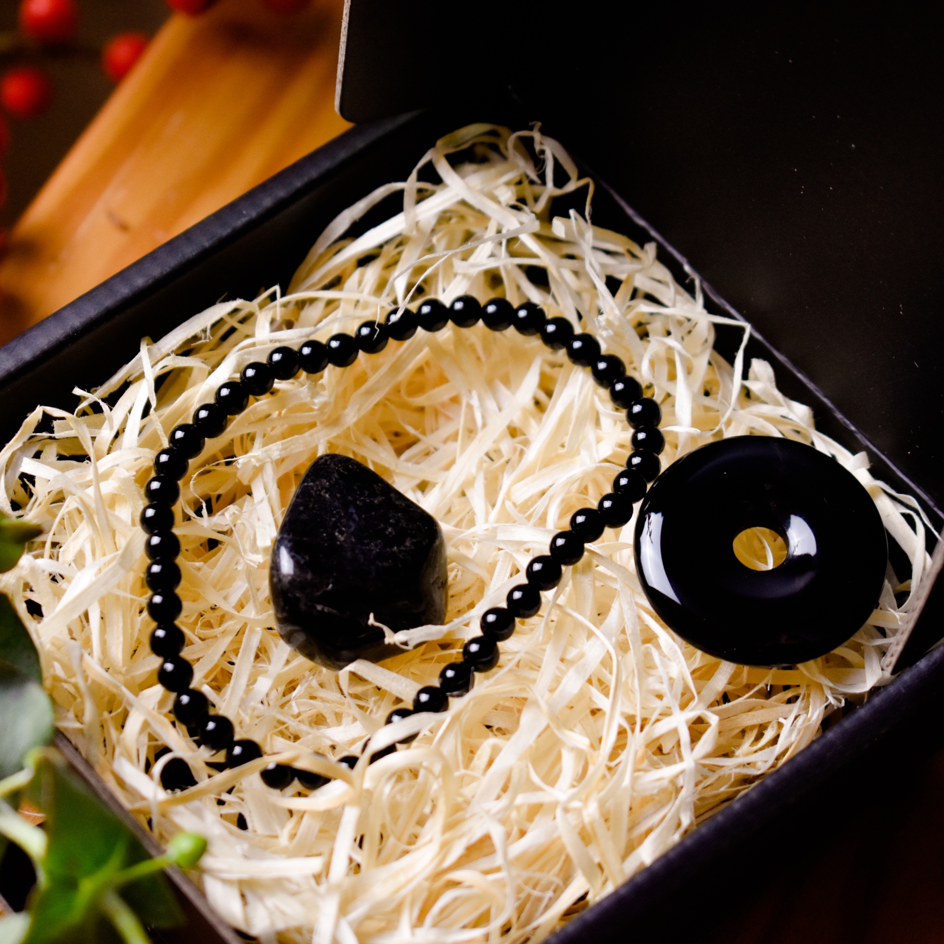 Mystic Treasure Box: Ónix | força e proteção Caixa preta aberta com joalharia em pedra preta sobre enchimento de palha de madeira