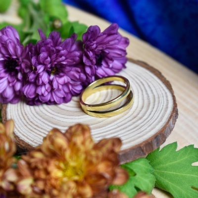Dois anéis dourados sobre madeira com flores roxas e castanhas ao redor
