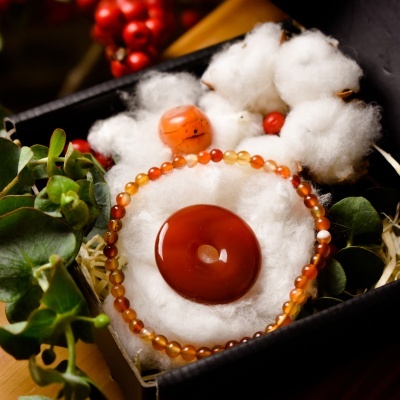 Conjunto de pulseira e pendente em tom laranja e castanho numa caixa com algodão e plantas