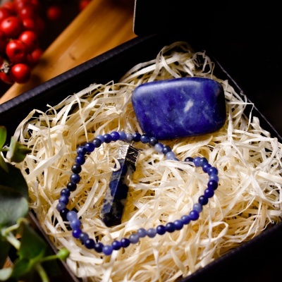 Conjunto de joias com pulseira e pedra azul numa caixa preta com enchimento de palha