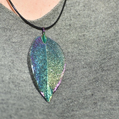 Colar com pendente em folha brilhante azul, verde e roxo numa camisola cinzenta
