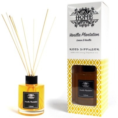 Reed diffuser bottle with amber liquid and black label next to yellow patterned box with product text