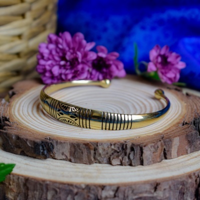 Pulseira dourada com padrões gravados sobre tronco de árvore com flores ao fundo