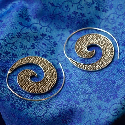 Brincos em espiral metálicos sobre tecido azul com padrão floral.