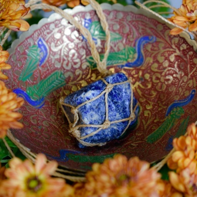 Bola de pedra azul com corda dentro de tigela decorativa vermelha com flores e flores laranja ao redor