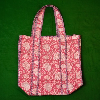 Saco de tecido vermelho com padrão floral branco e alças com costura azul sobre fundo verde