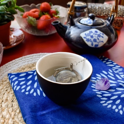 Chávena preta com infusor de chá e bule preto em mesa vermelha com morangos